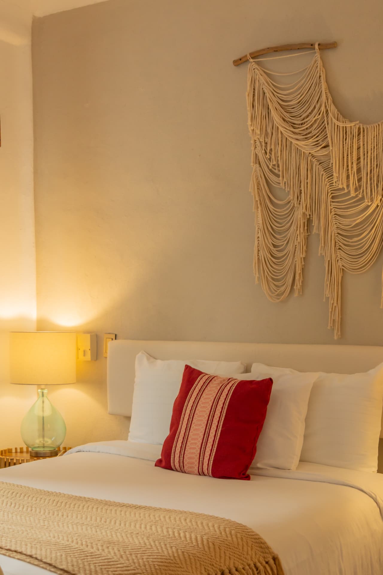Cama de la habitación 107 con cojín rojo tejido y macramé