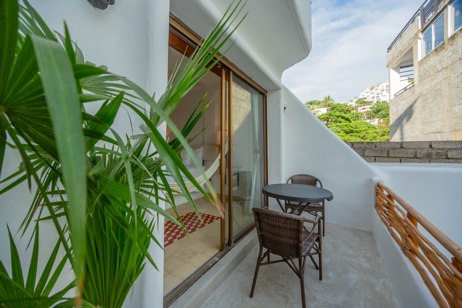 Balcón de la habitación 208 enmarcado por palmeras con vista al vecindario