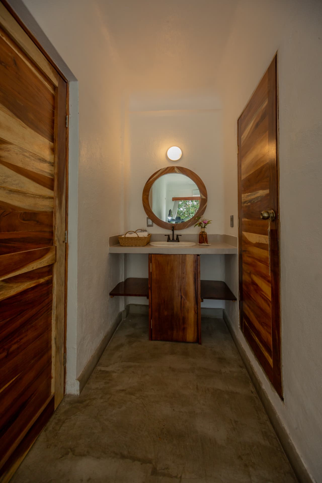 Bathroom hallway in room 105 with vanity, round mirror and wood doors