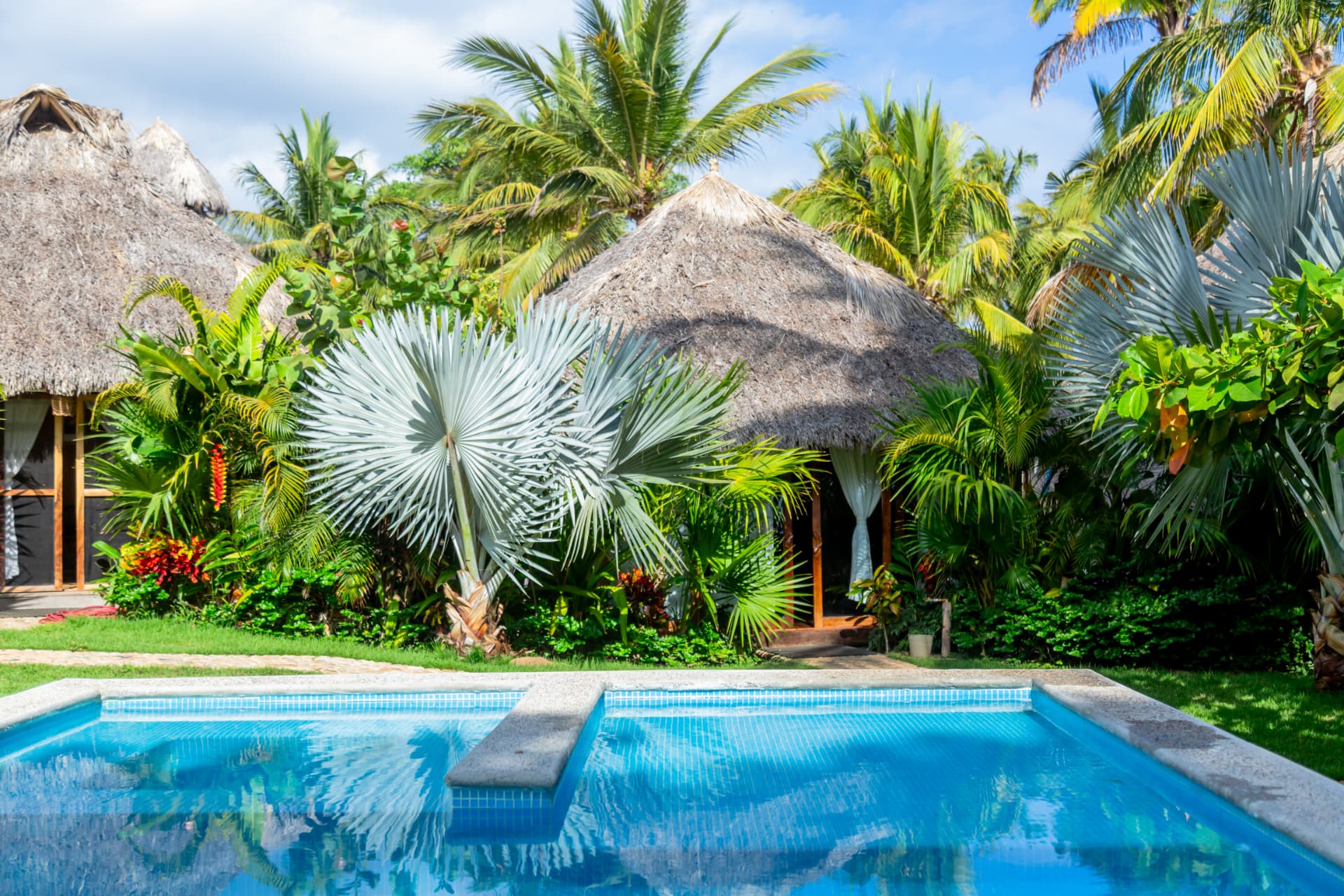 Villas con palapa entre jardines frente a la alberca