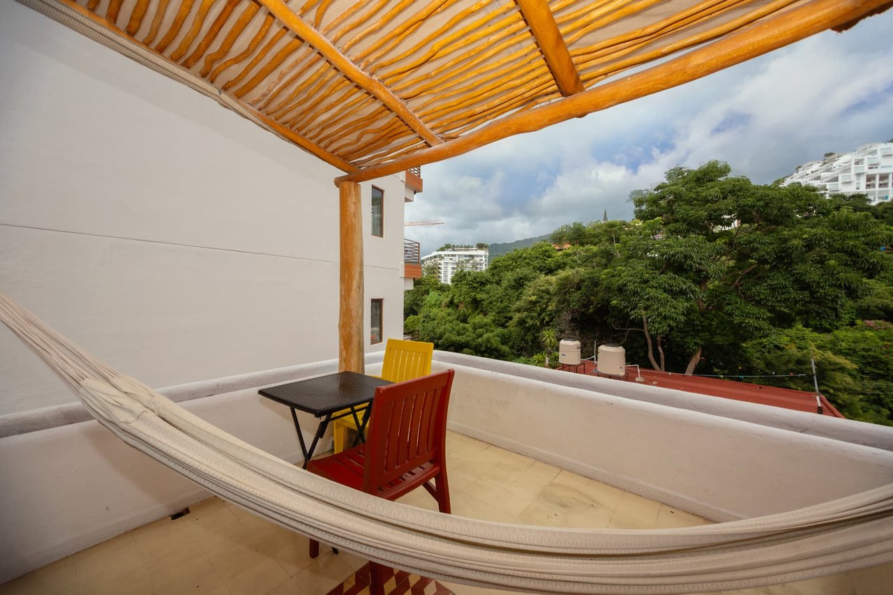 Balcony in room 307 with hammock, table and colorful chairs under a wood pergola