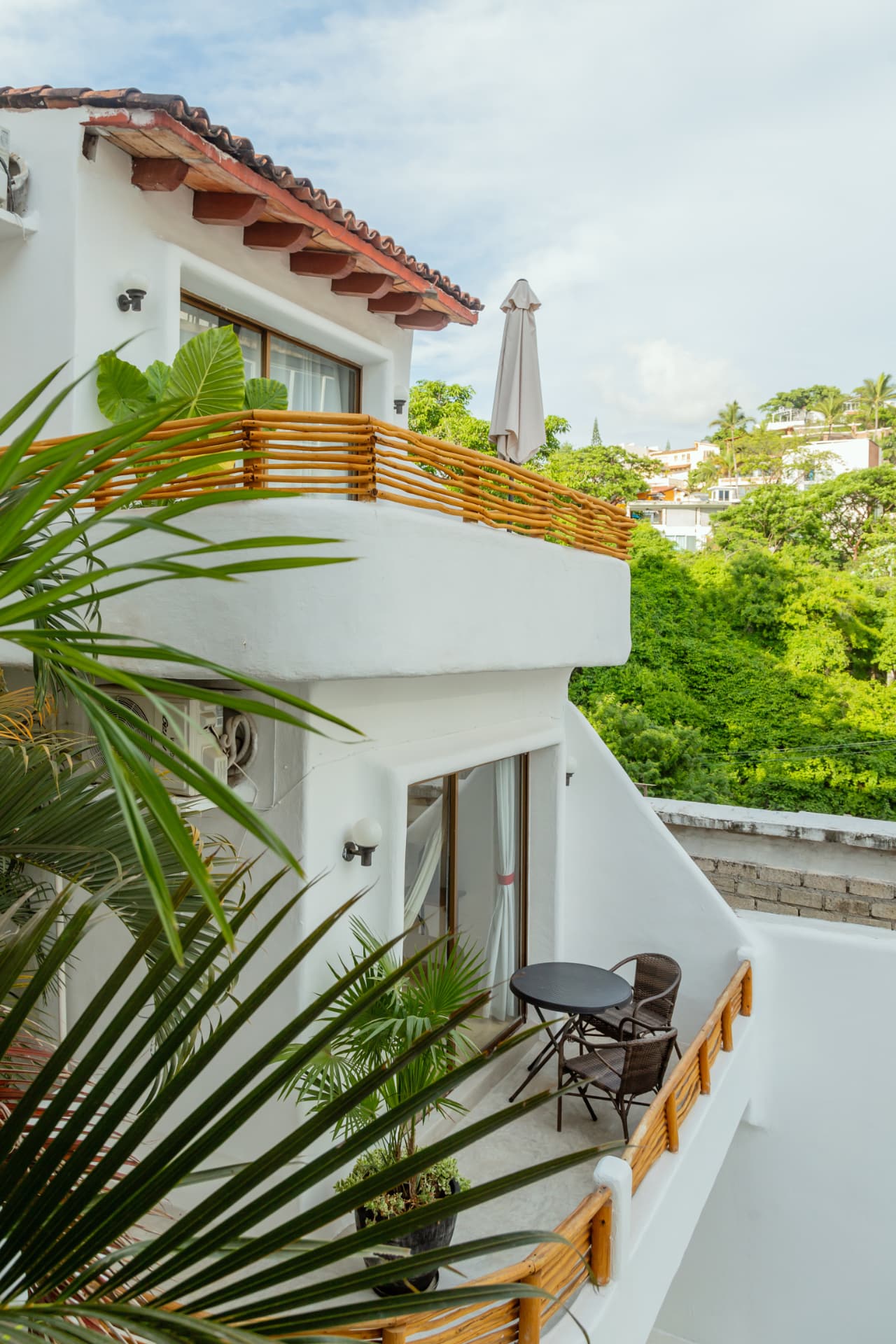 Balcón exterior de la habitación 308 con mesa, sillas y vista a los tejados y la vegetación