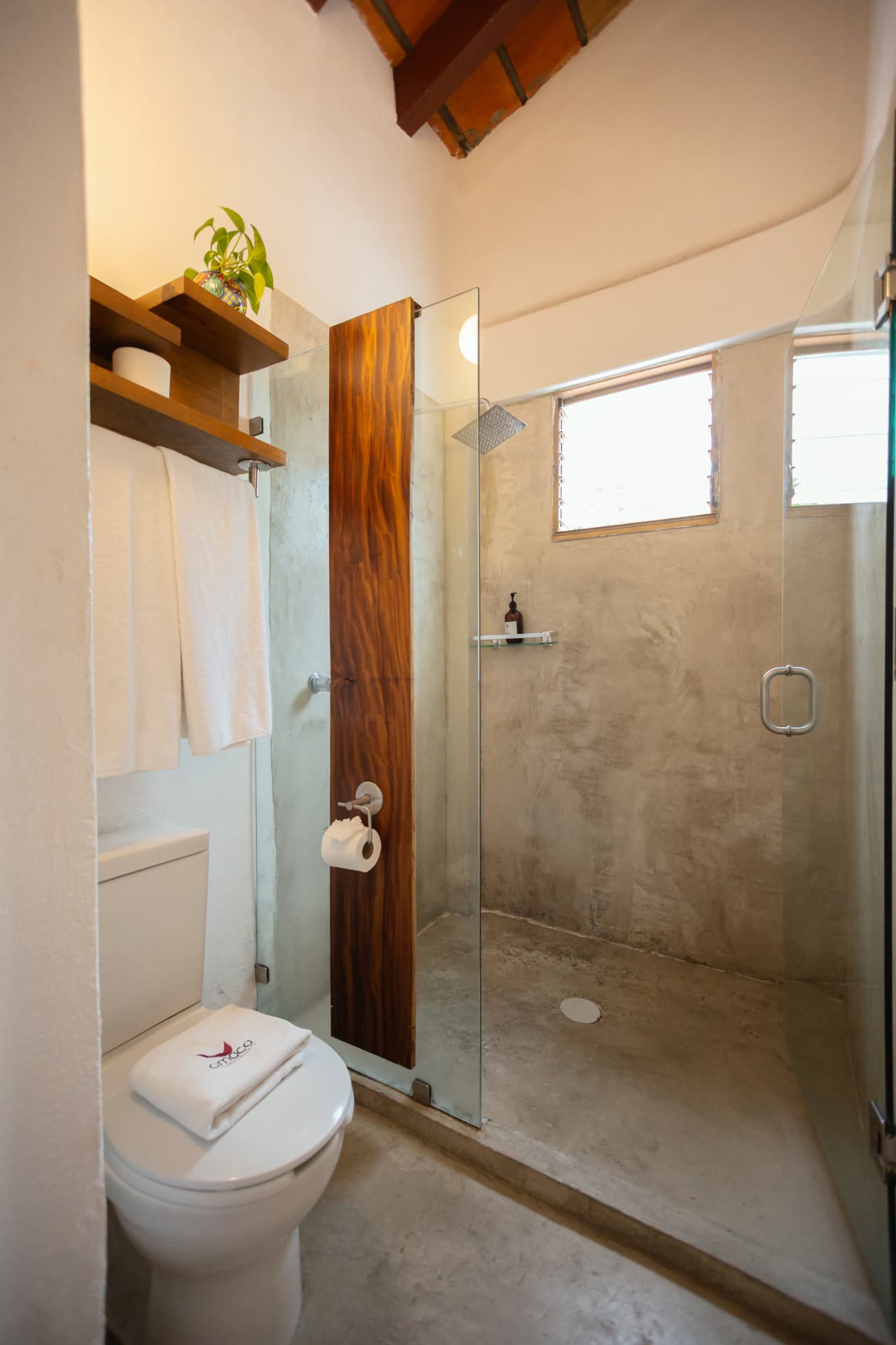 Baño de la habitación 308 con regadera de concreto, puerta de vidrio y ventana de madera