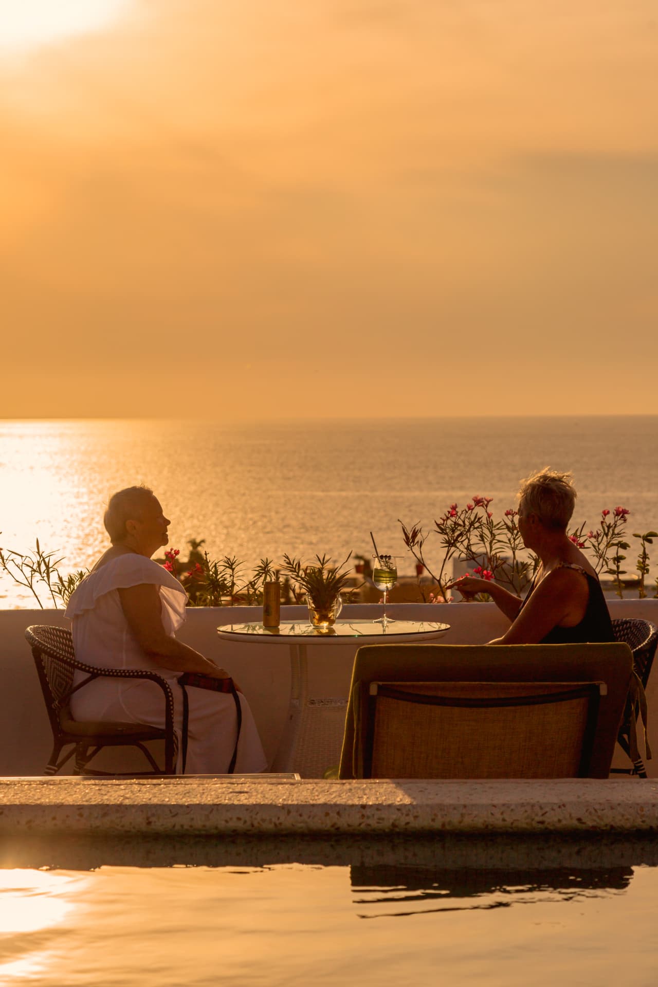 Dos huéspedes conversando junto a la alberca durante el atardecer dorado