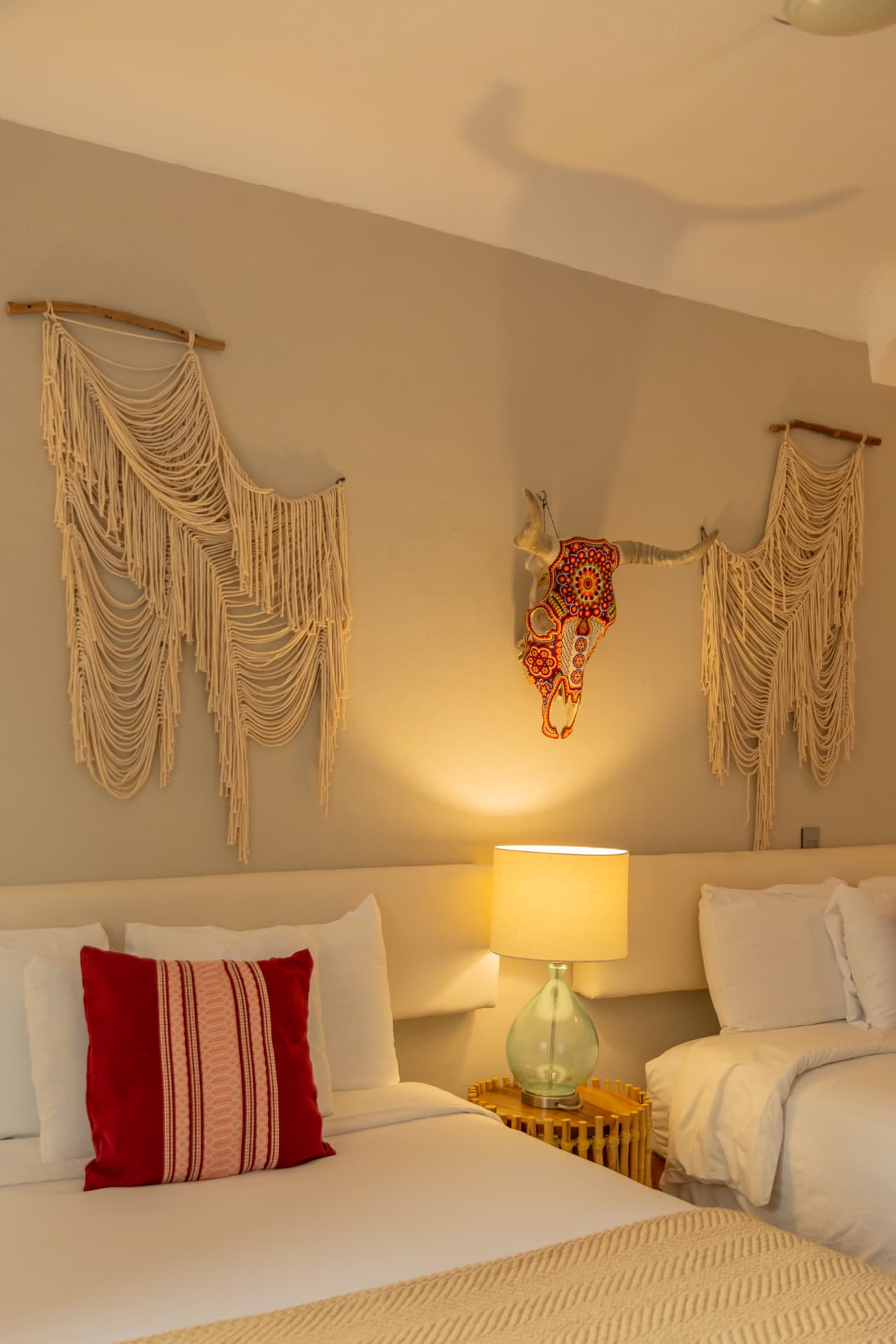 Detalle de cama con cojín rojo y macramé en la habitación 107