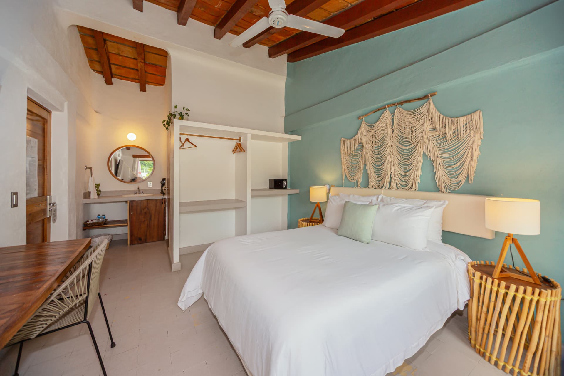 Vista amplia de la habitación 308 con cama Queen, pared azul, macramé, ropero abierto y escritorio