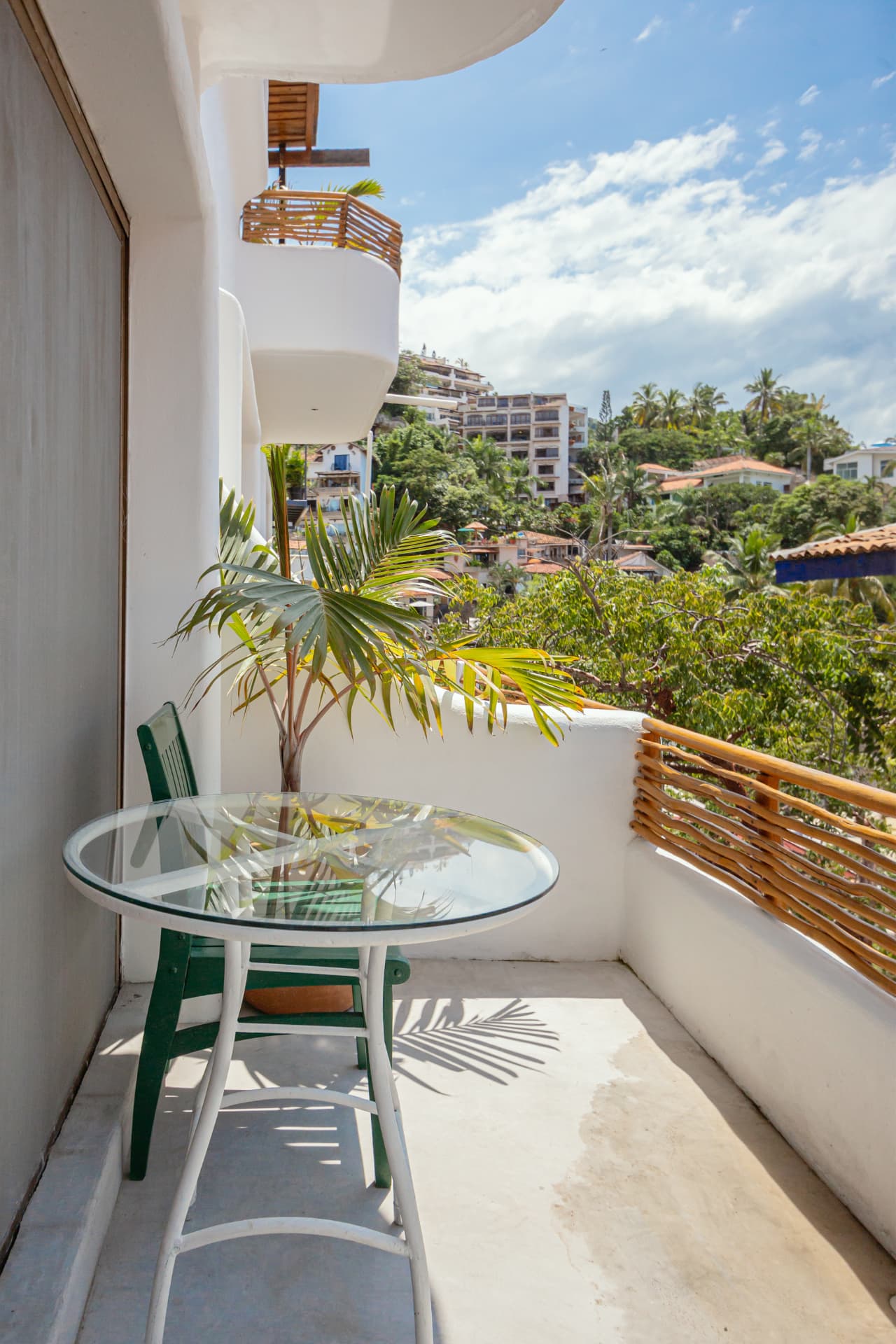 Balcony of Room 203 with glass table, green chair and tropical greenery views