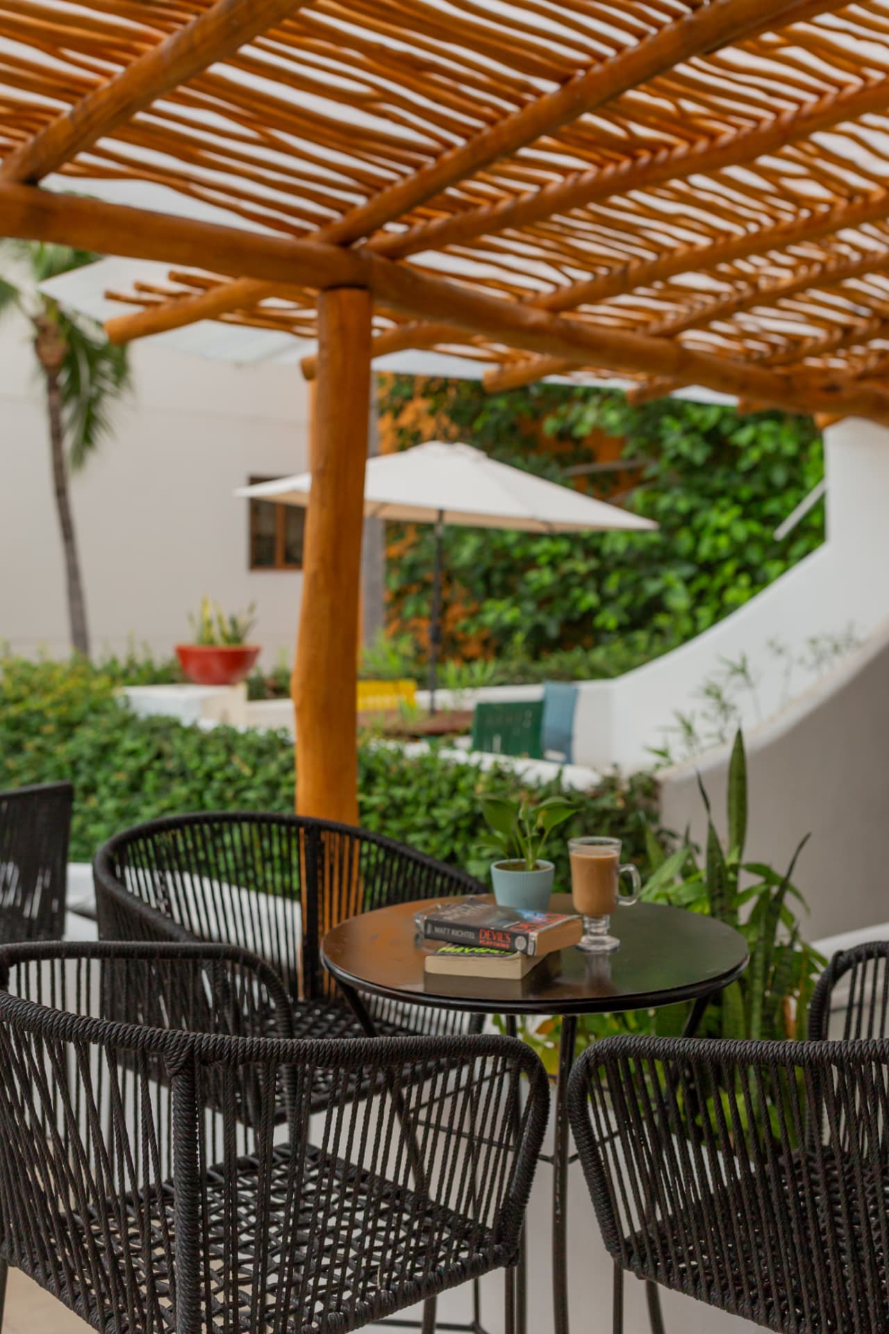 Terraza de café bajo una pérgola de madera con vegetación al fondo