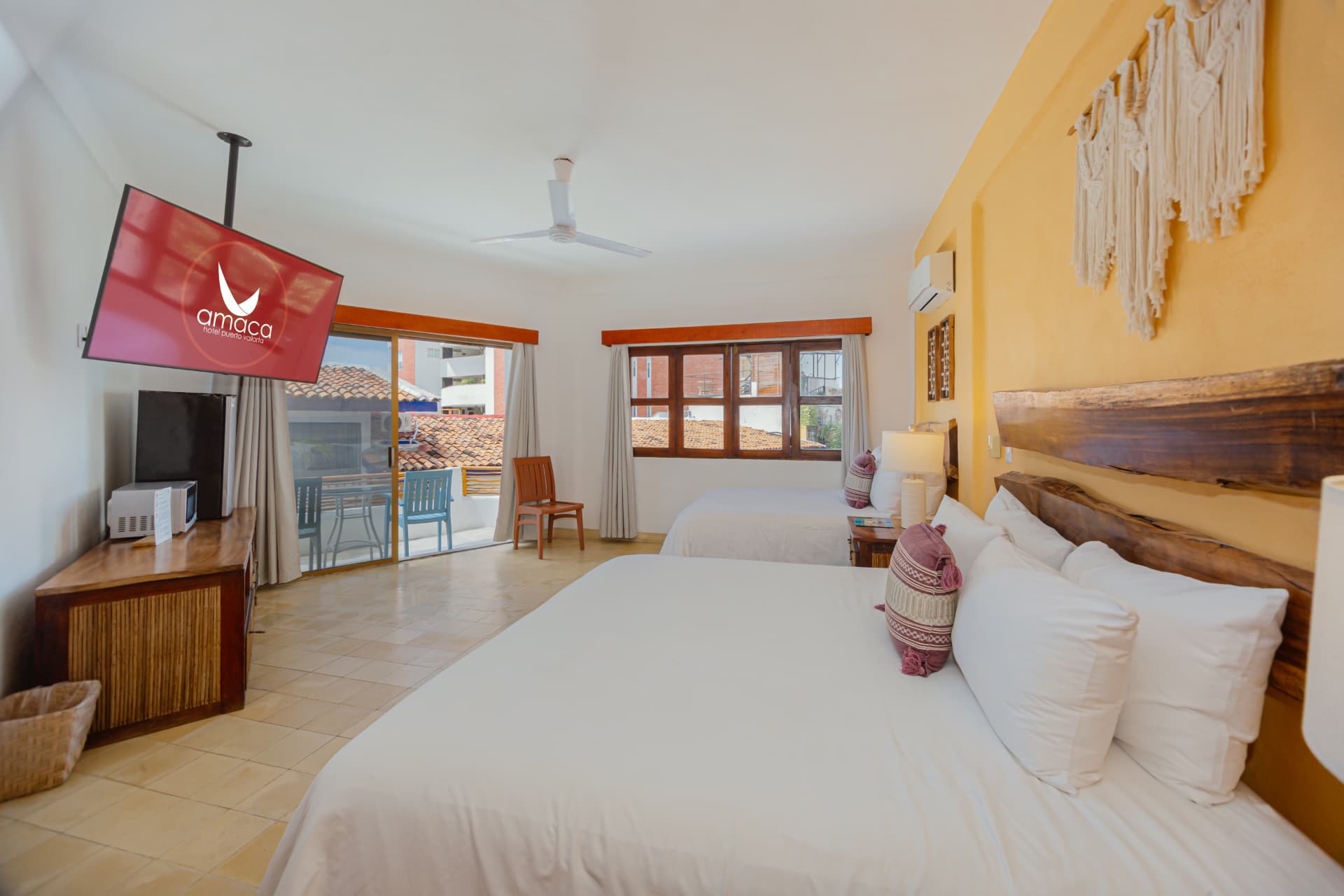 Room 203 with the two beds, yellow wall, macrame and access to the terrace with colorful chairs