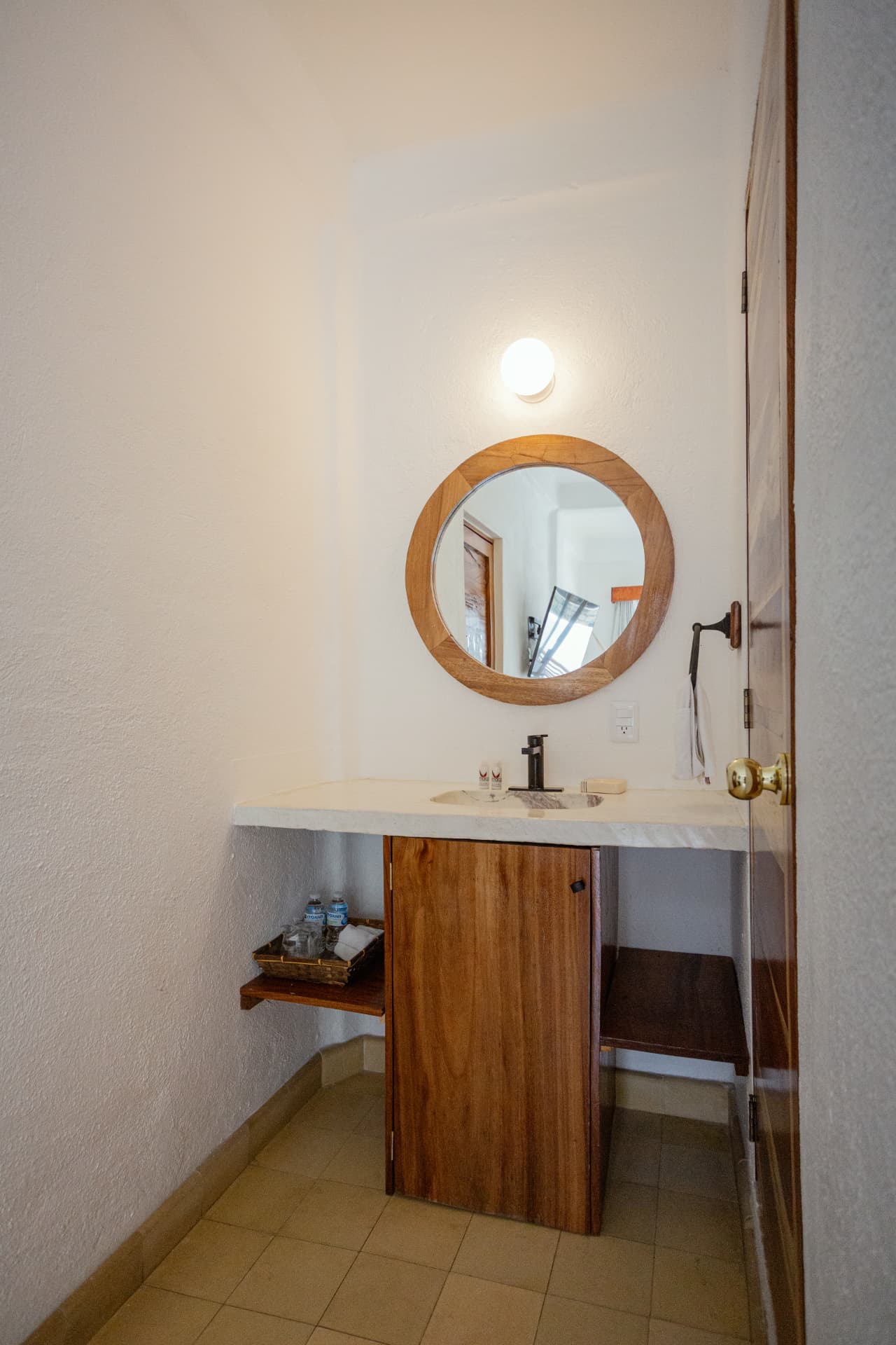 Lavabo de la habitación 208 con espejo redondo de madera y puerta de madera