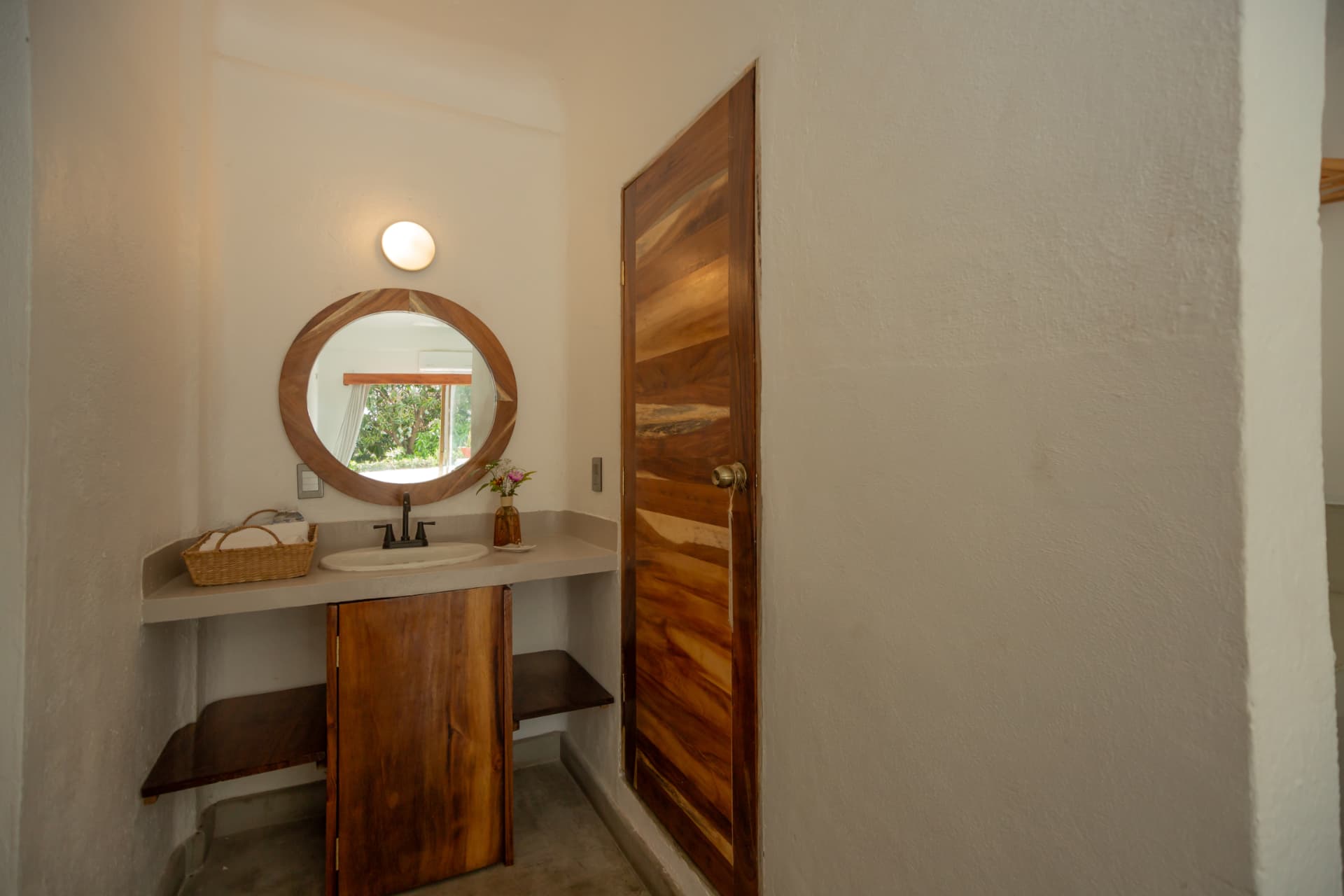 Habitación 105: área de lavabo con espejo redondo y carpintería de madera