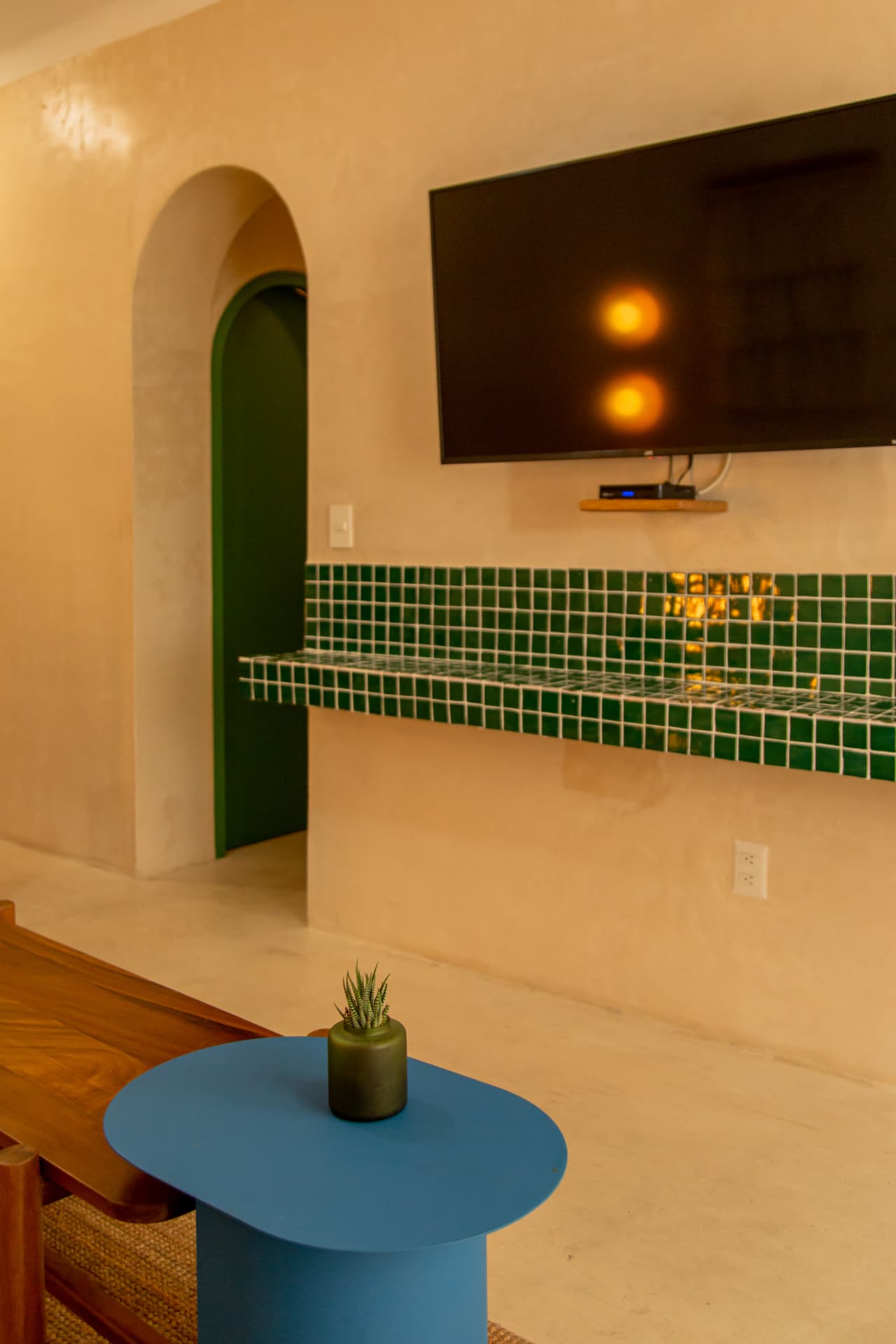 Common area of Amaca Residence with television, blue table, wood and green mosaics