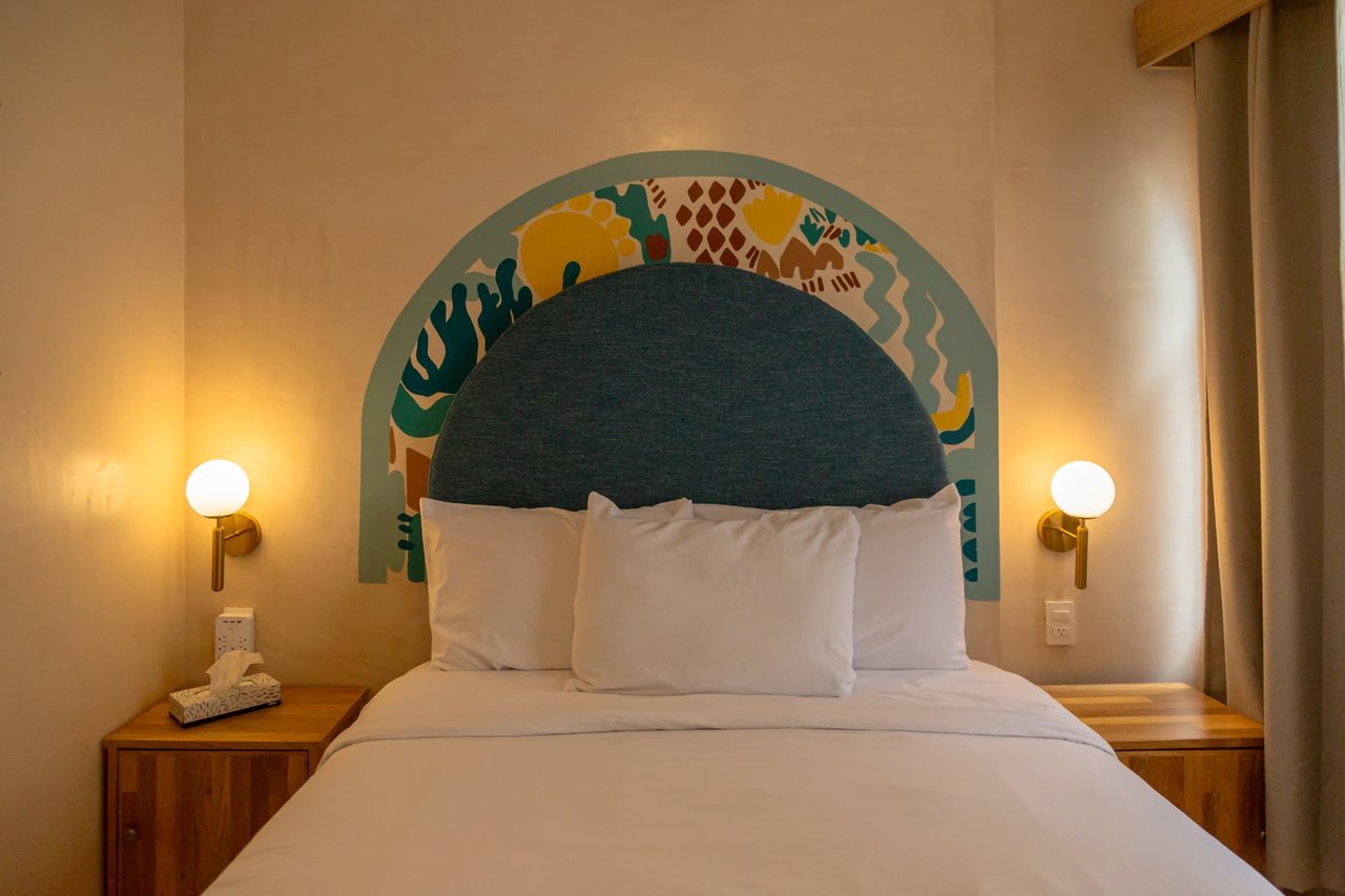 Queen bed of Amaca Residence with blue headboard and handcrafted mural