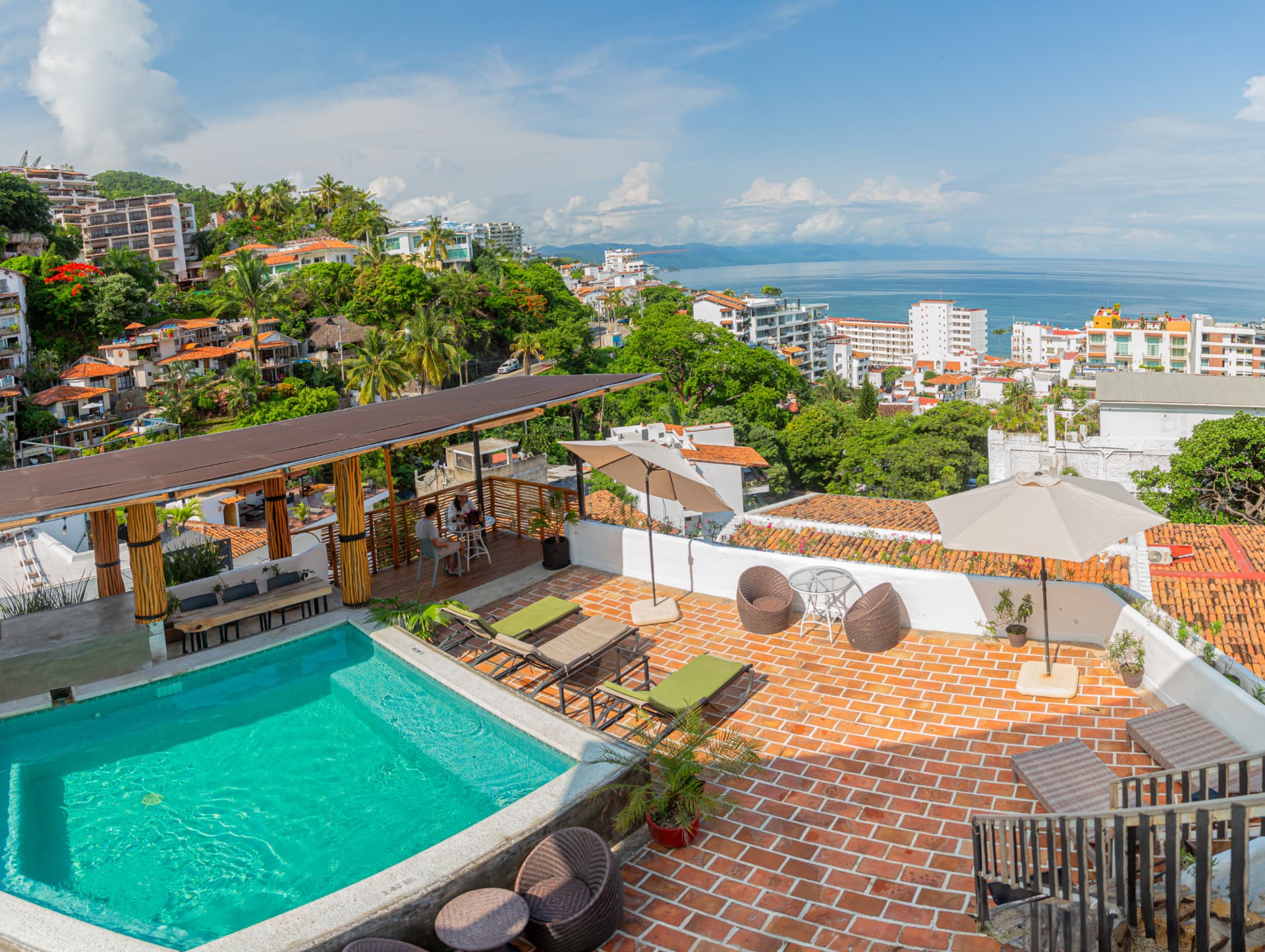 Alberca turquesa del rooftop con camastros y la Bahía de Banderas al fondo