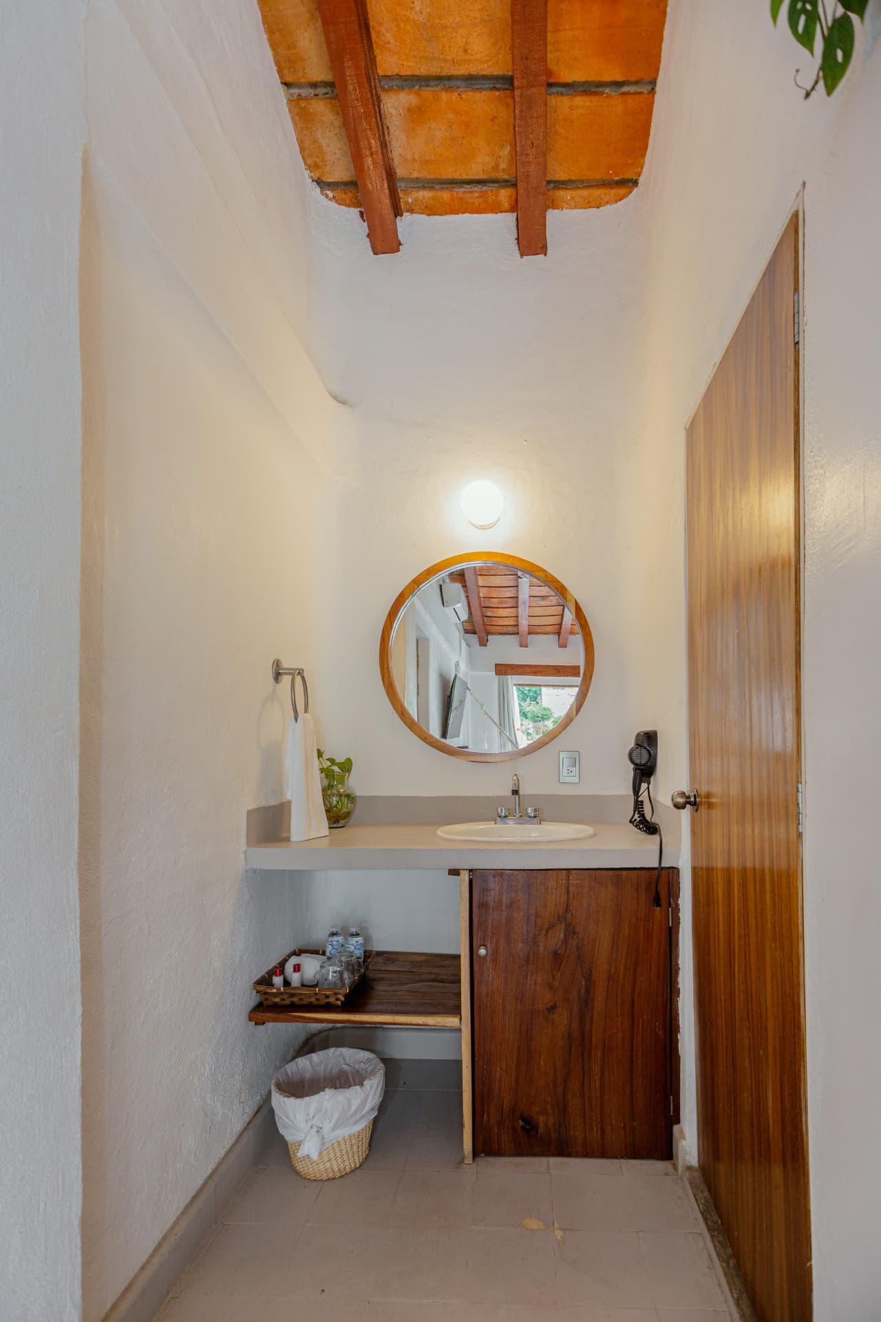 Lavabo de la habitación 308 con espejo redondo de madera y puerta de madera