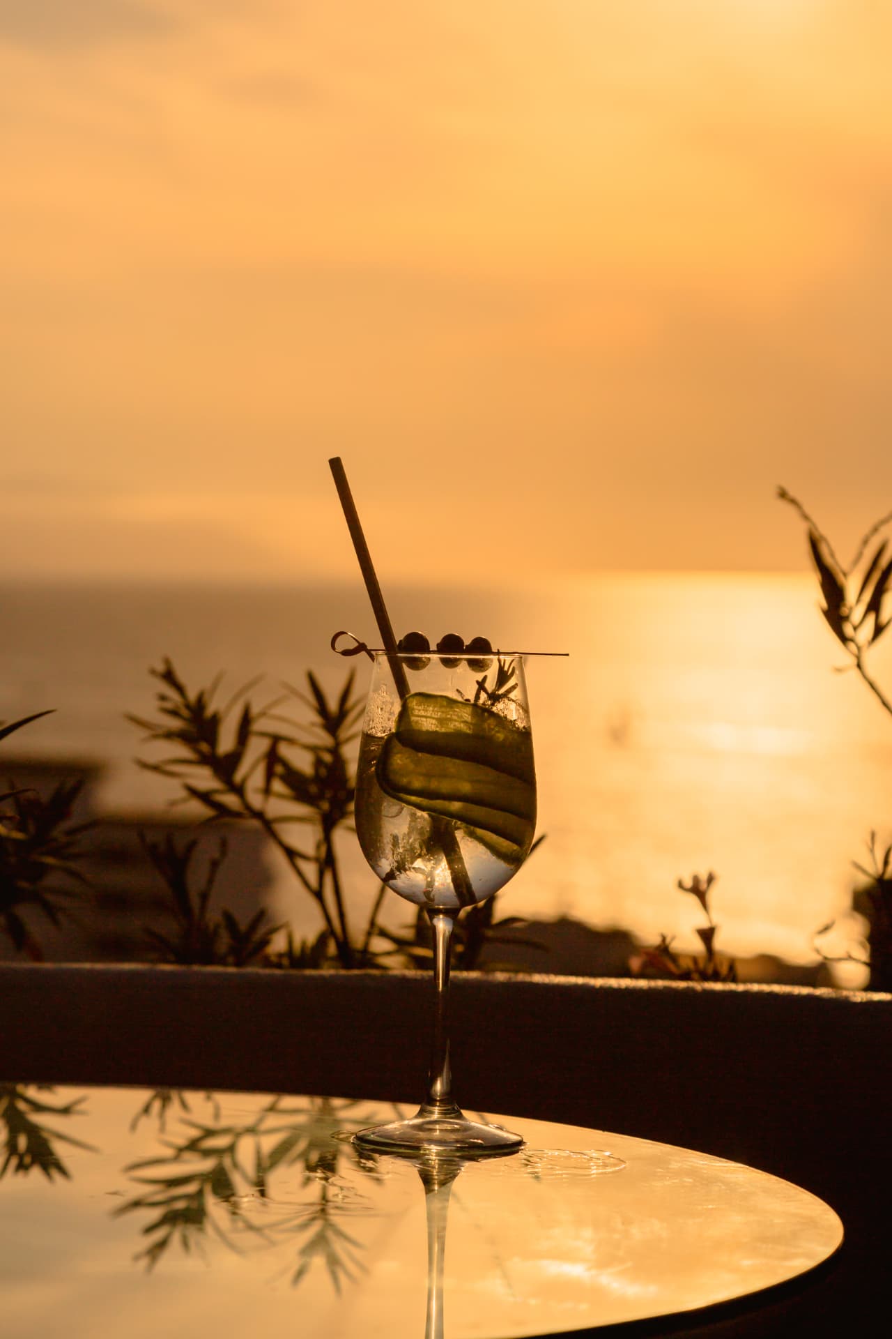 Cóctel de pepino con aceitunas frente al sol poniente en el mar