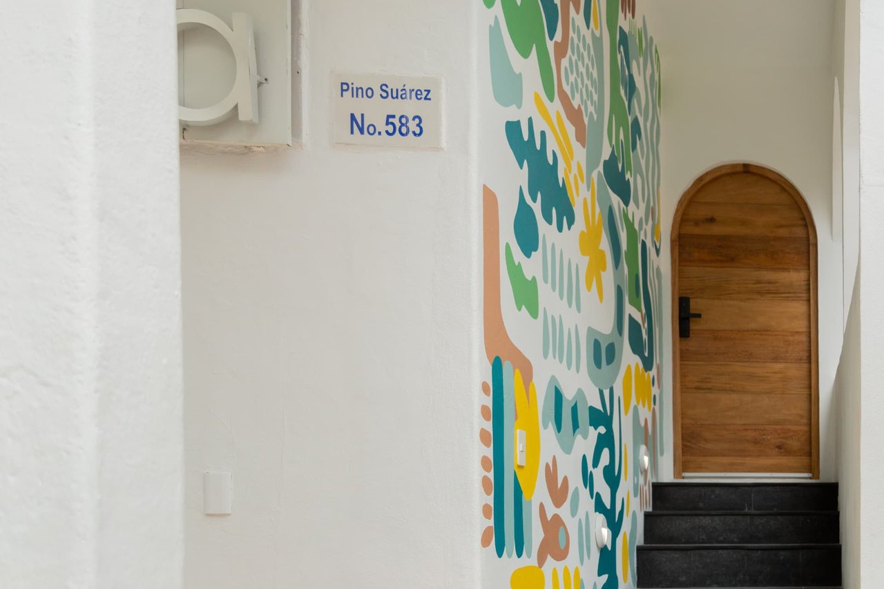Independent entrance of Amaca Residence with colorful mural and curved wooden door