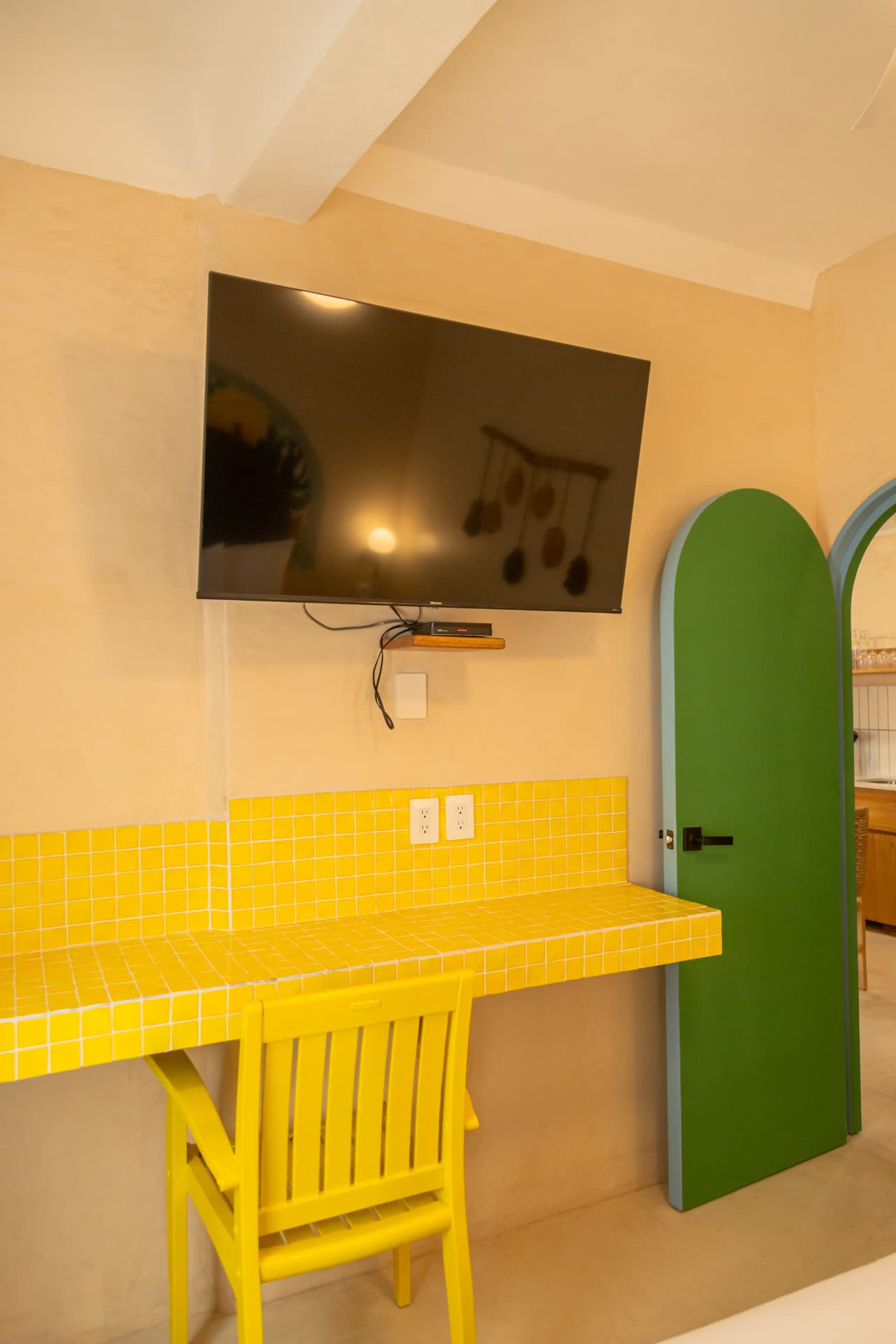 Desk with yellow mosaics, television and curved green door in Amaca Residence
