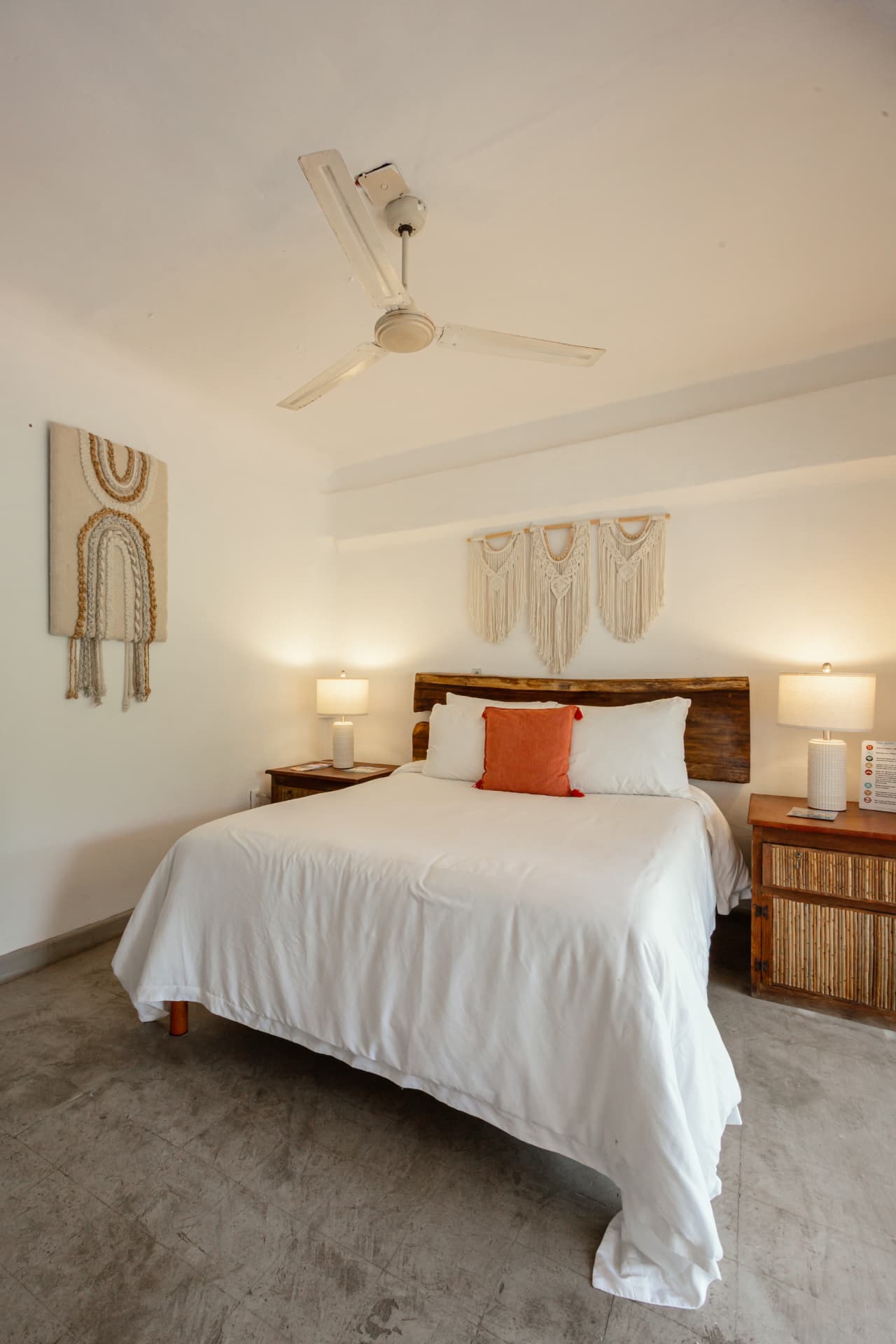 Cama Queen de la habitación 307 con cabecera de madera, lámparas y macramé