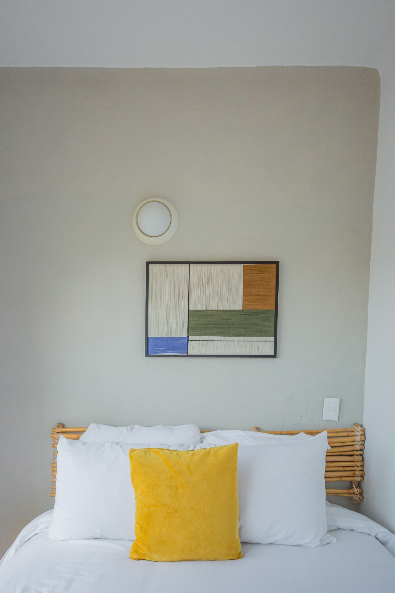 Habitación 202: detalle de la cama con cojín amarillo y cuadro textil